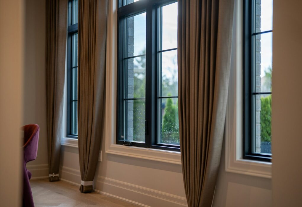 How to hang curtains to make windows look bigger: floor-length taupe drapes hung high and wide beside tall black-framed windows