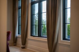 How to hang curtains to make windows look bigger: floor-length taupe drapes hung high and wide beside tall black-framed windows
