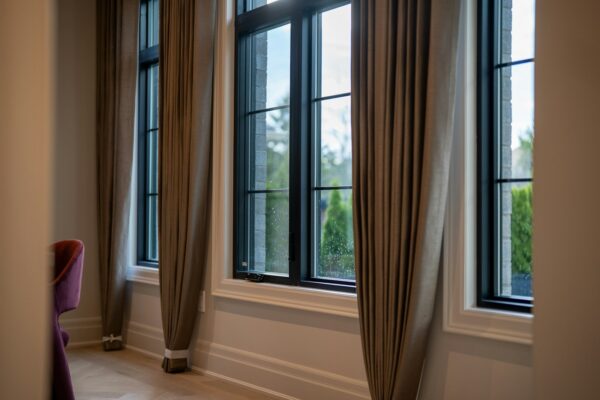 How to hang curtains to make windows look bigger: floor-length taupe drapes hung high and wide beside tall black-framed windows